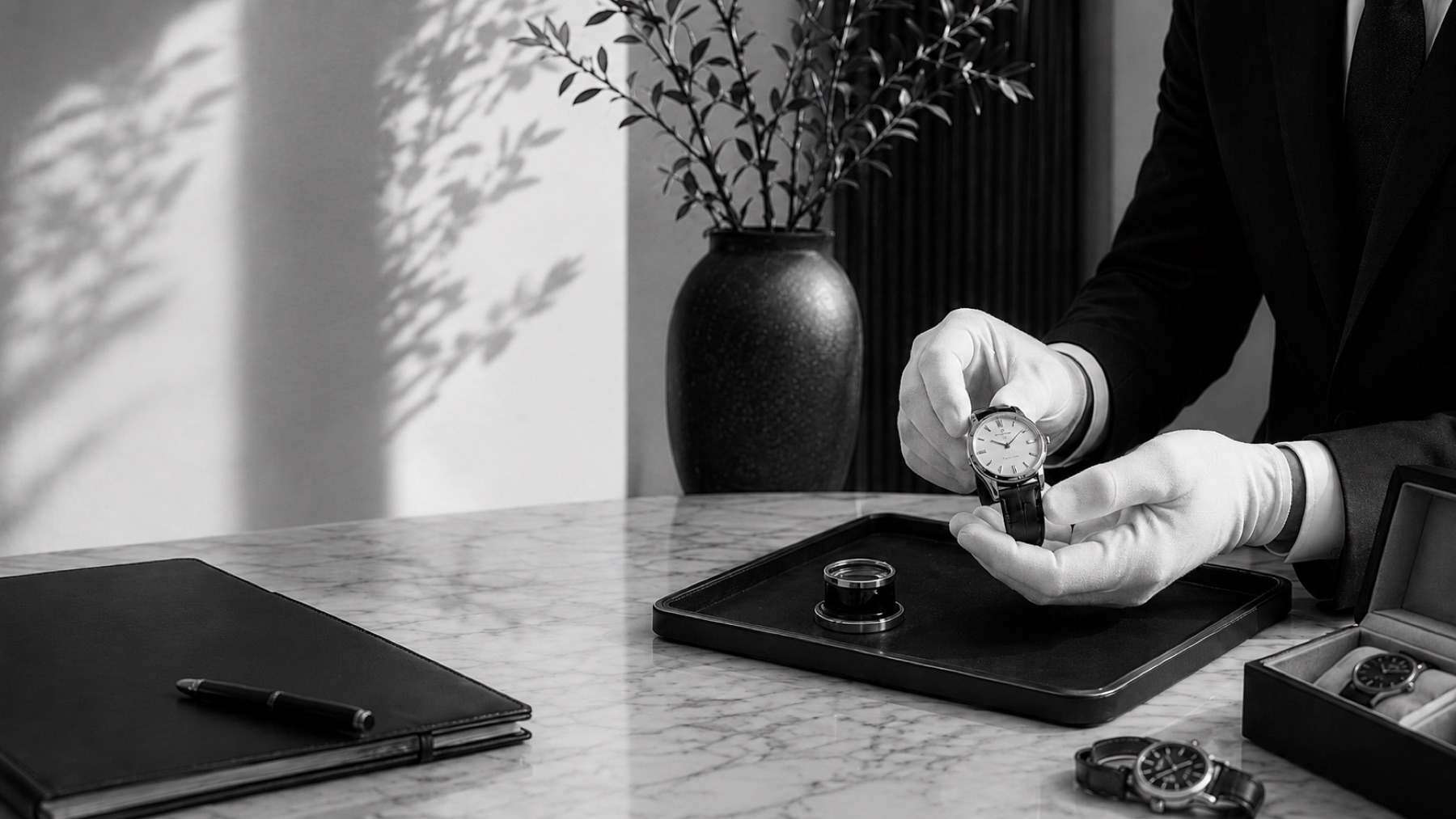 A gloved specialist presenting a timepiece at a marble desk